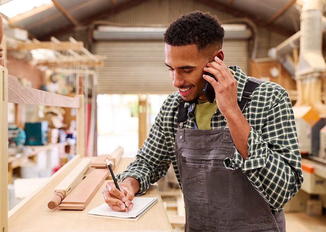 A carpenter taking a customer's order inquiry over a phone call in a furniture work shop.