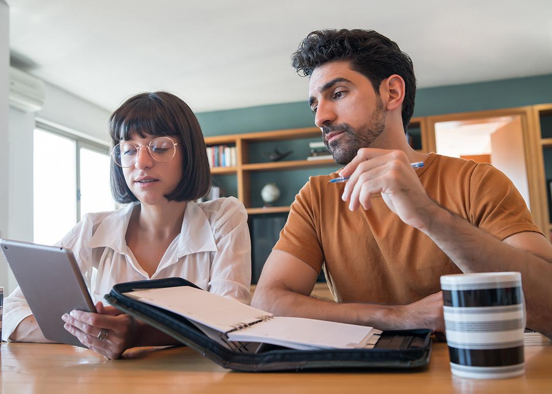 A young couple reviews and pays bills online using a digital tablet.