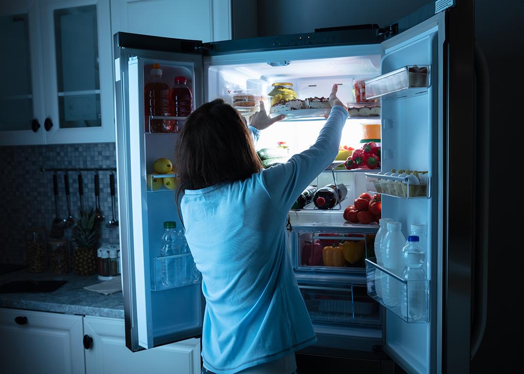 Woman storing food in the refrigerator at night.