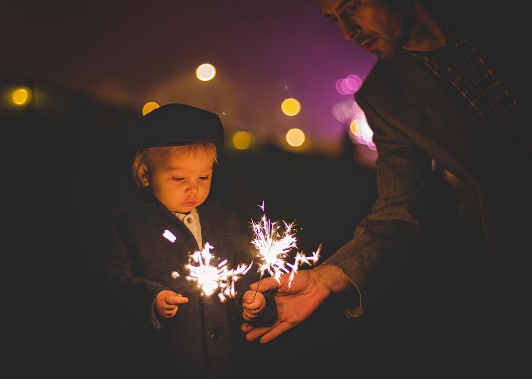 A father helping his young child with sparklers during a New Year celebration.