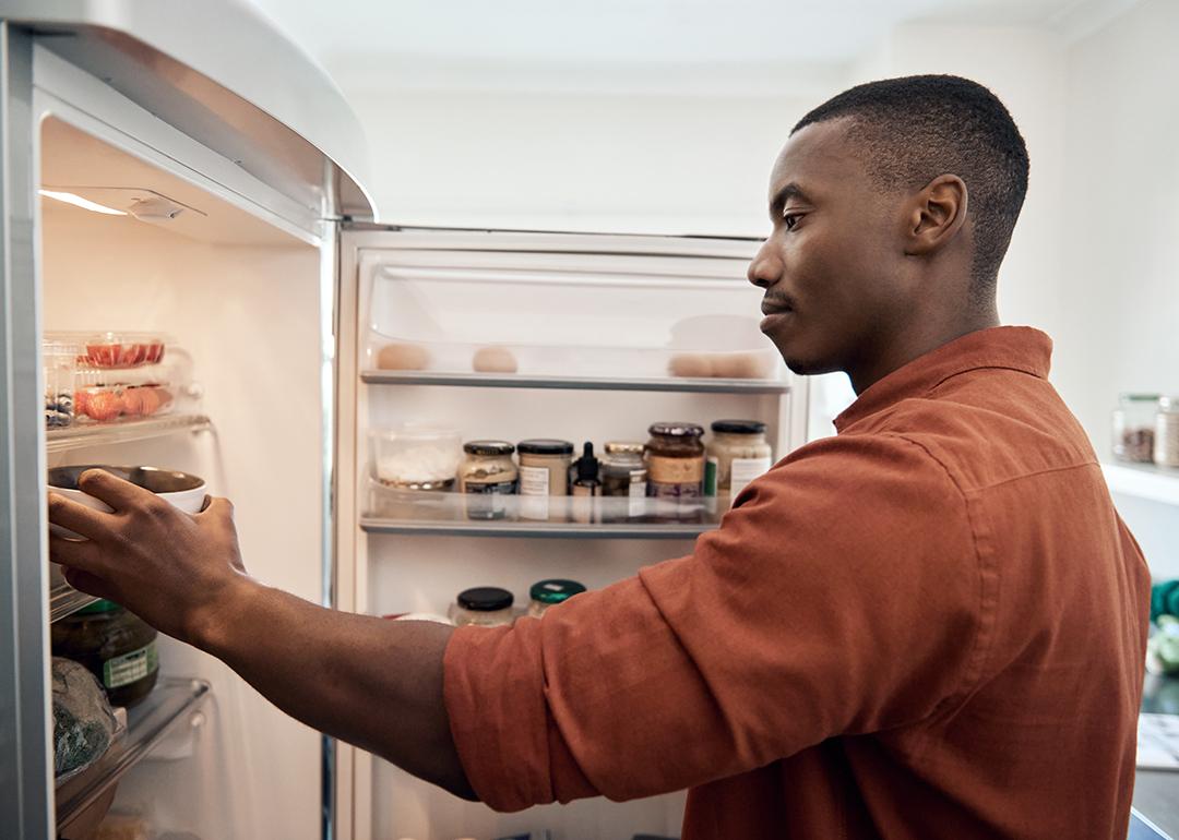 A person checking food items inside a refrigerator from the kitchen.