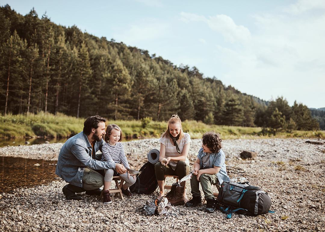 A family camping beside a small creek and cooking fish over a campfire.