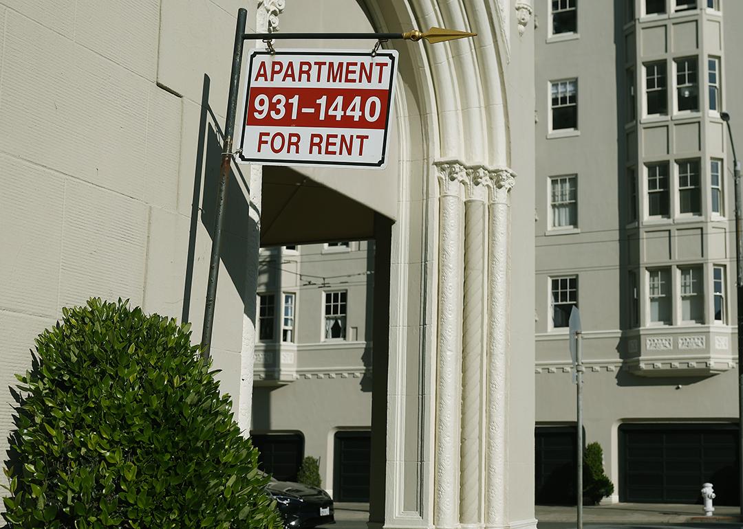 An 'apartment for rent' sign hangs outside of an apartment building.