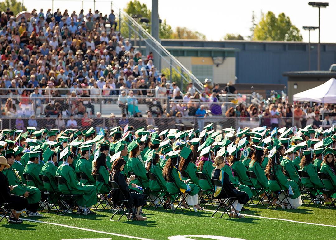  A high school graduation ceremony happening outdoors in the campus' sports field.