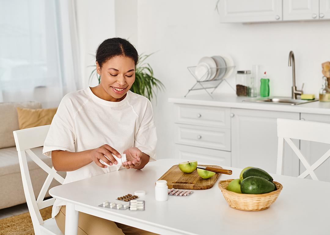 A nutritionist taking food supplements alongside eating fresh fruits at home.