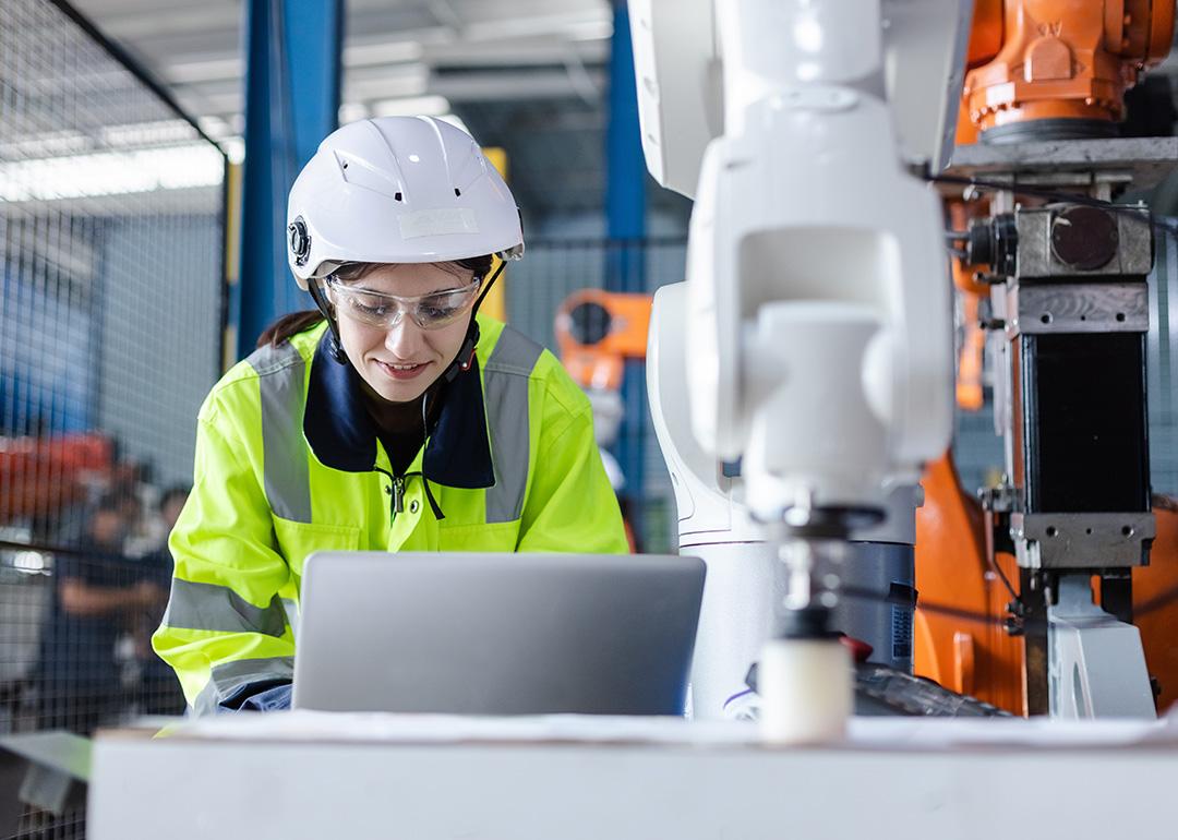 An engineer checking automation robotics from a laptop for a manufacturing machine in an industrial factory.