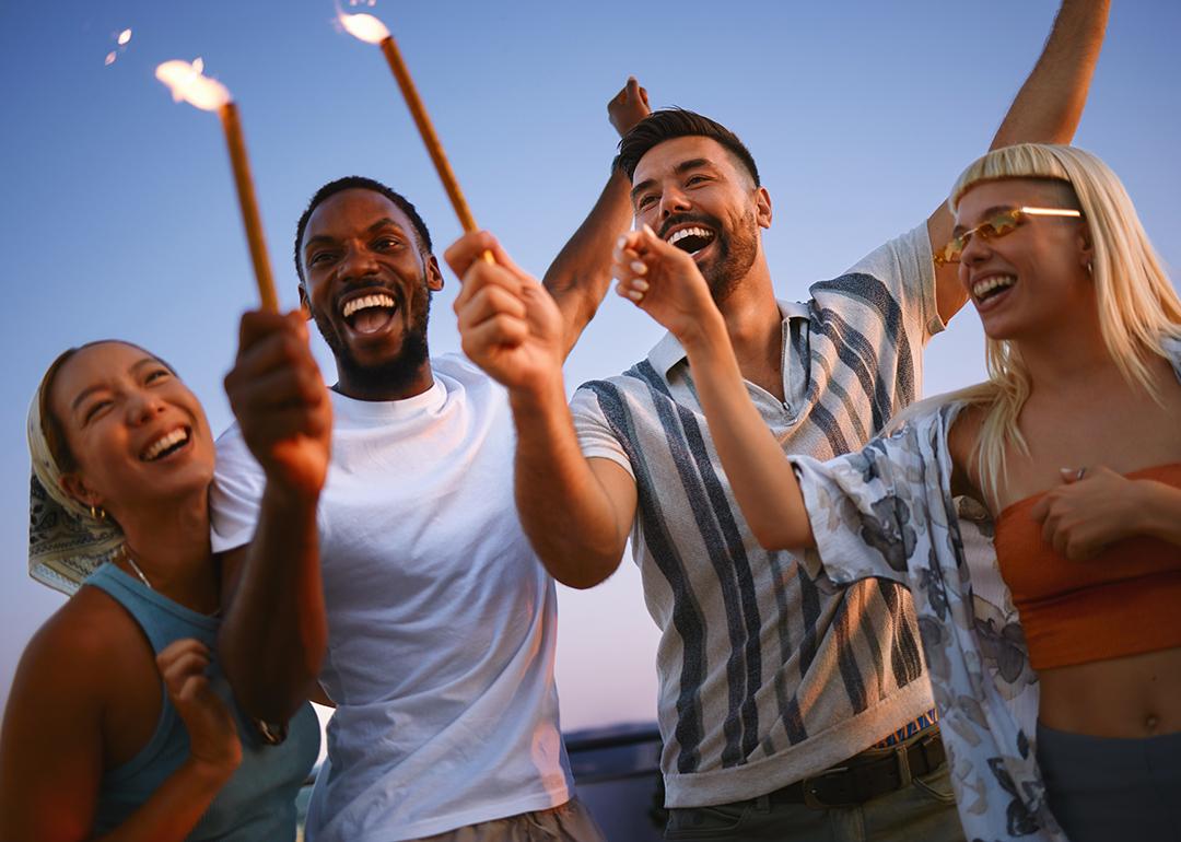 A group of friends celebrating together with sparklers during a rooftop party at sunset.