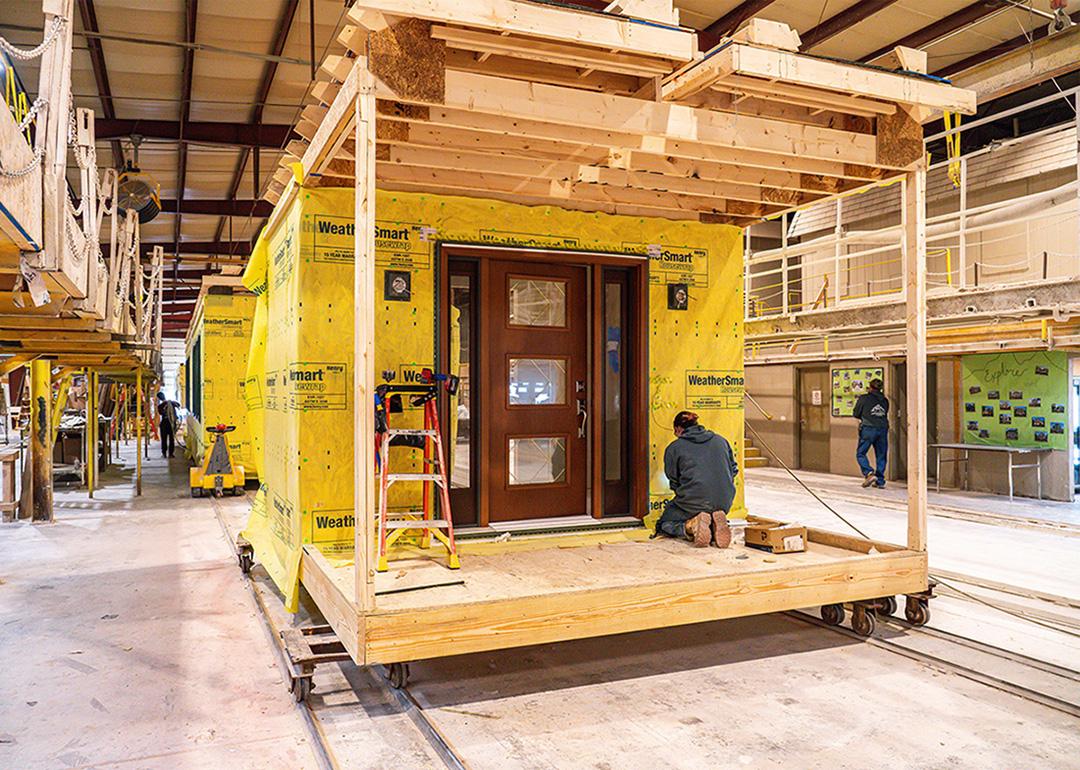 A worker kneels on a wooden platform building a modular home under construction in a factory in Middleburg, Pennsylvania.