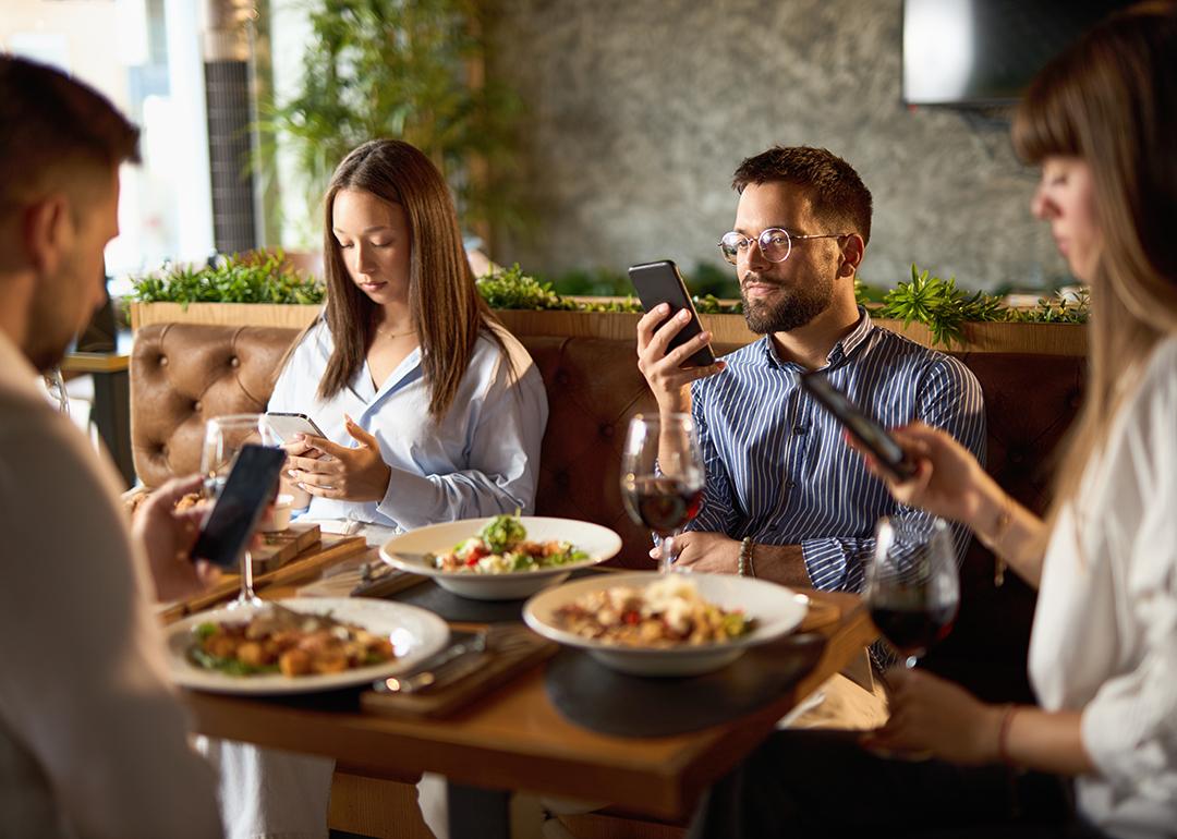 A group of business colleagues checking their smartphones while eating lunch in a restaurant.