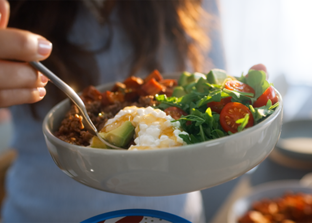 A woman holding a bowl of salad with cottage cheese.
