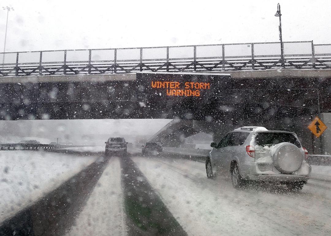 Windshield POV of a car passing under a bridge with an electronic 'Winter Storm Warning' sign.