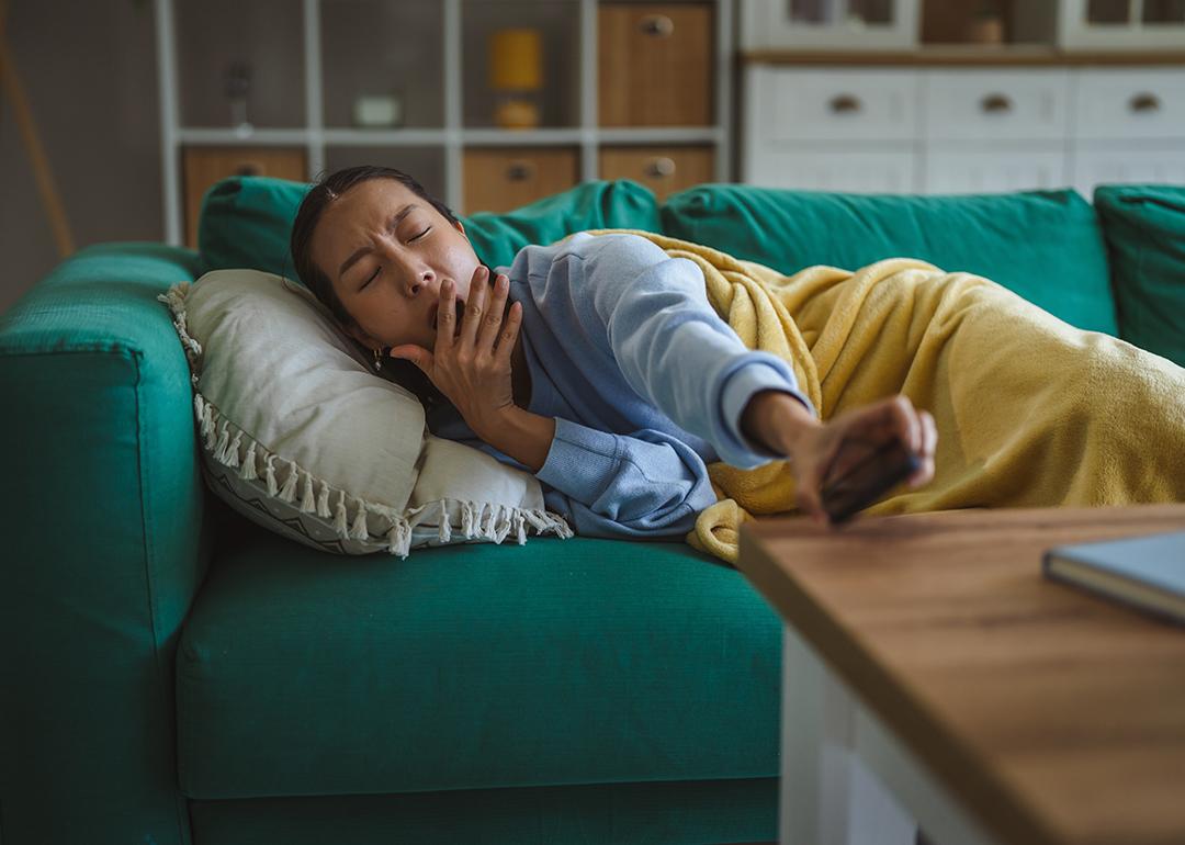 A young woman at home yawning and lying comfortably on a green couch.