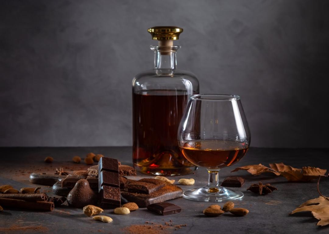 A glass of cognac, cognac in a bottle and pieces of chocolate on a dark background.