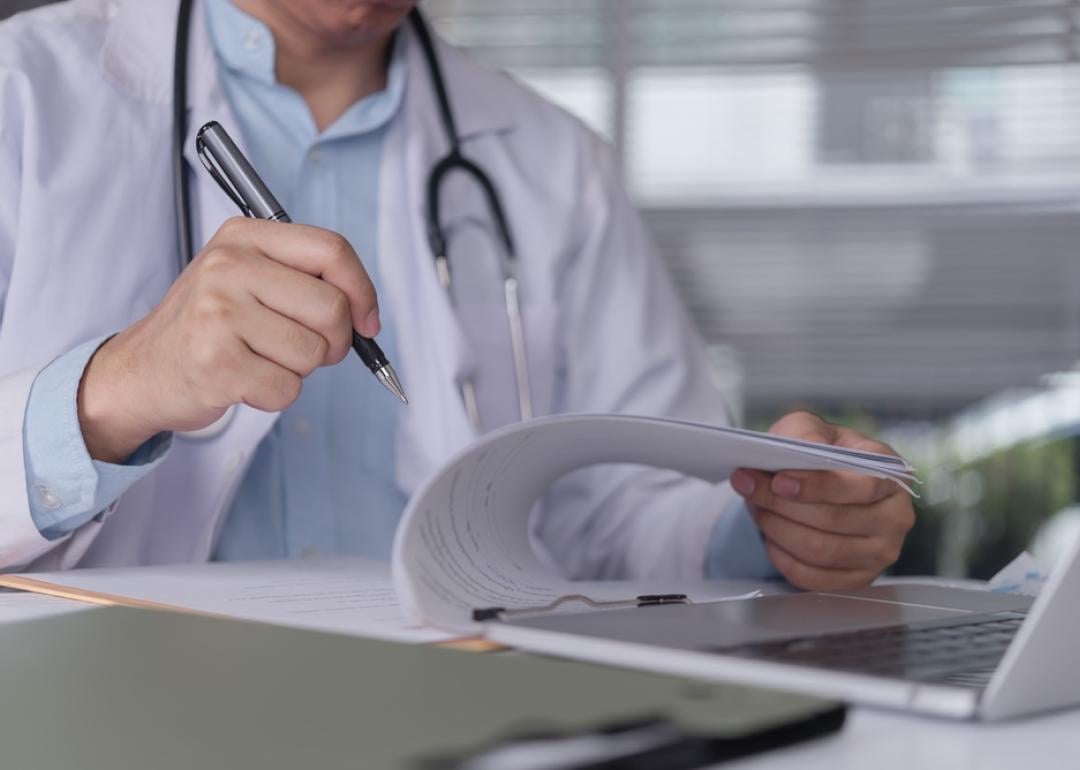 Doctor hand writing medical report on clipboard.