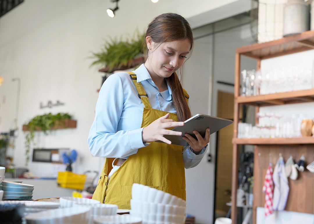 A shopkeeper checking inventory stocks of pottery and tableware from a work tablet device.