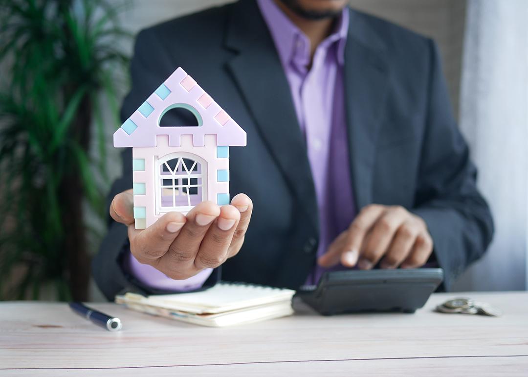 A finance professional holding a small figure of a house as a concept of investing in real estate.