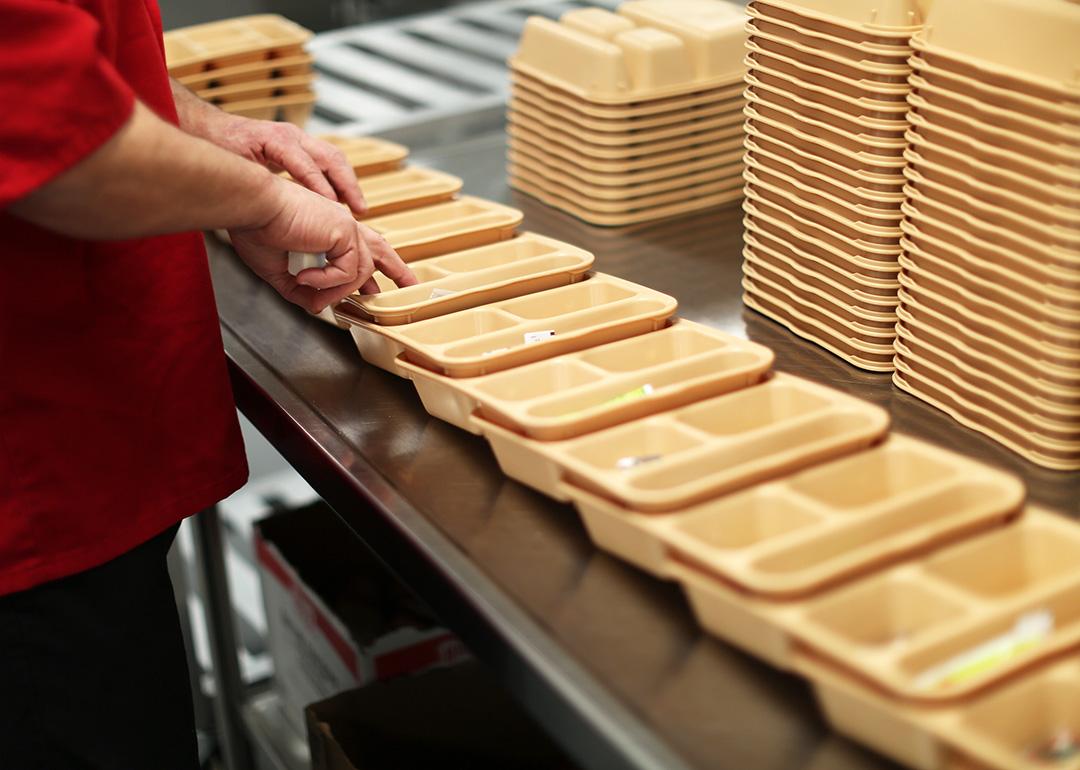 An inmate at Maine Correctional Center in Windham adds condiments to food trays in preparation for distribution throughout the facility. 