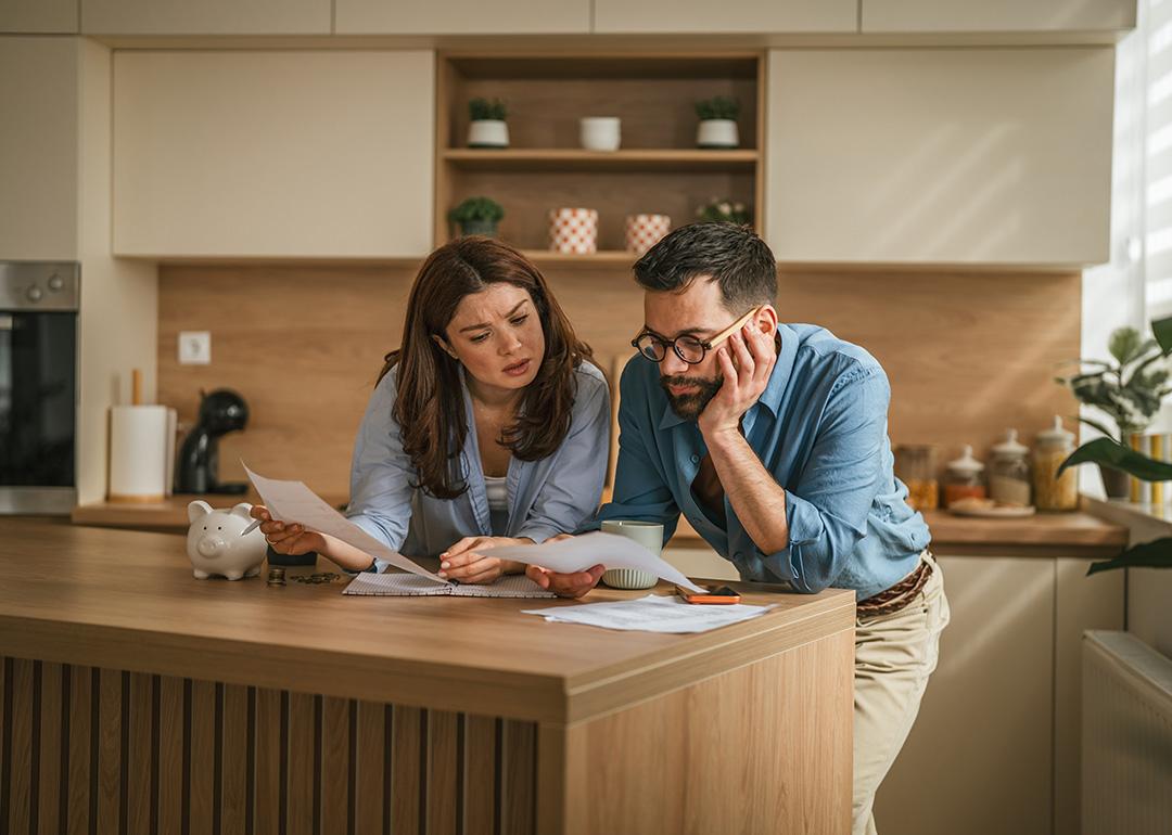 A couple reviewing bills and documents from their household finances at their home's kitchen.
