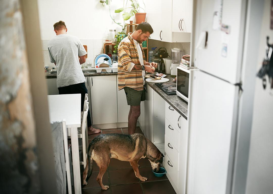 A young gay couple cooking together in their kitchen and feeding their dog.