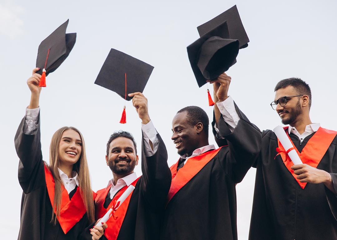 A group of graduates celebrate by holding their graduation caps in the air.