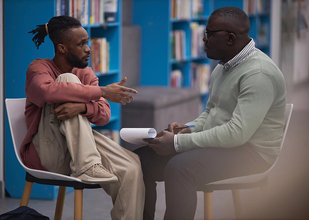 A young black male student talking to a counselor in their college library.