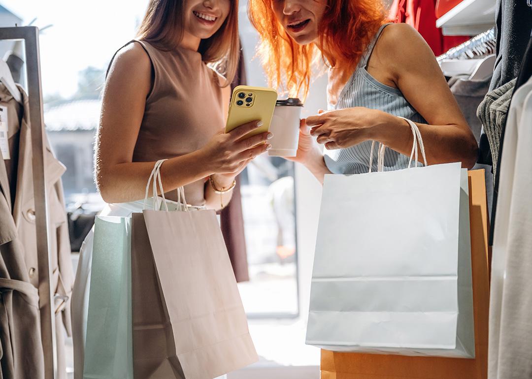 Two friends checking items' information from a smartphone after shopping clothes in a store.