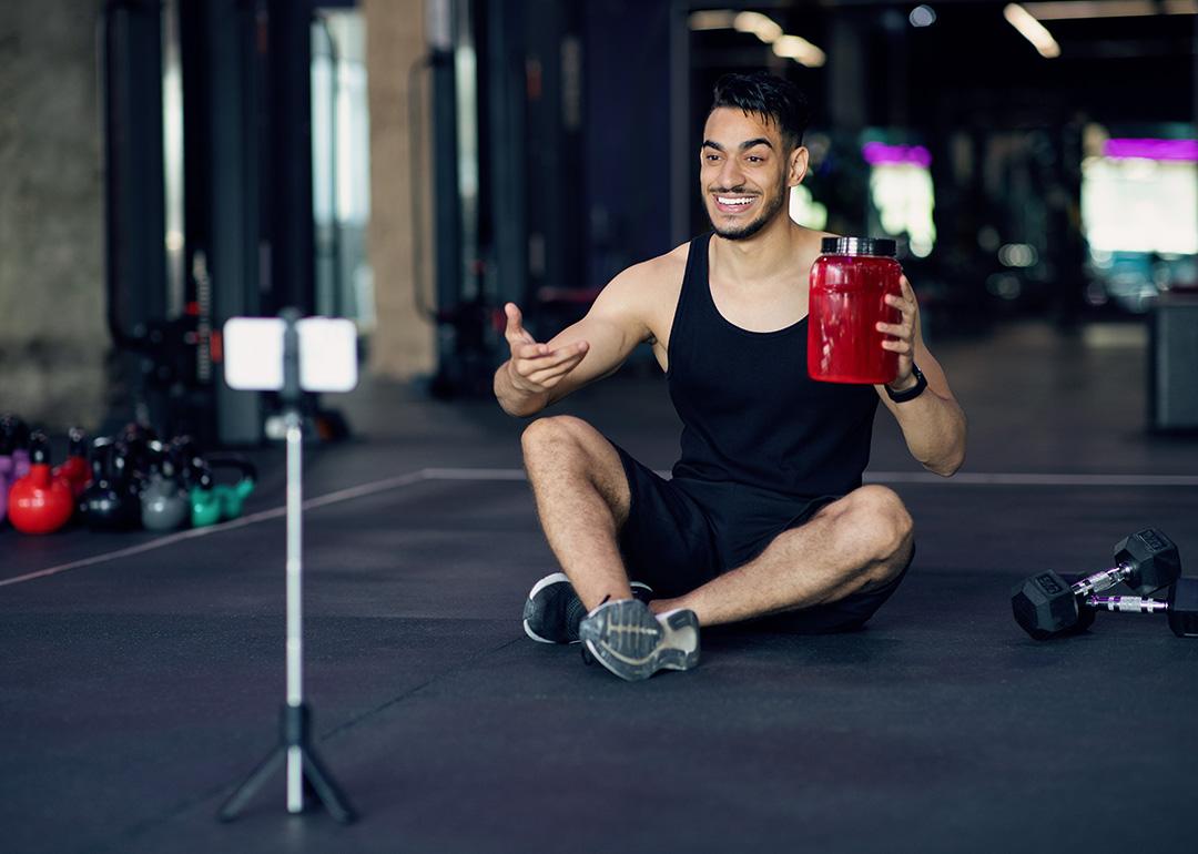 A fitness blogger recording himself from his smartphone at a gym for a sport wellness video.