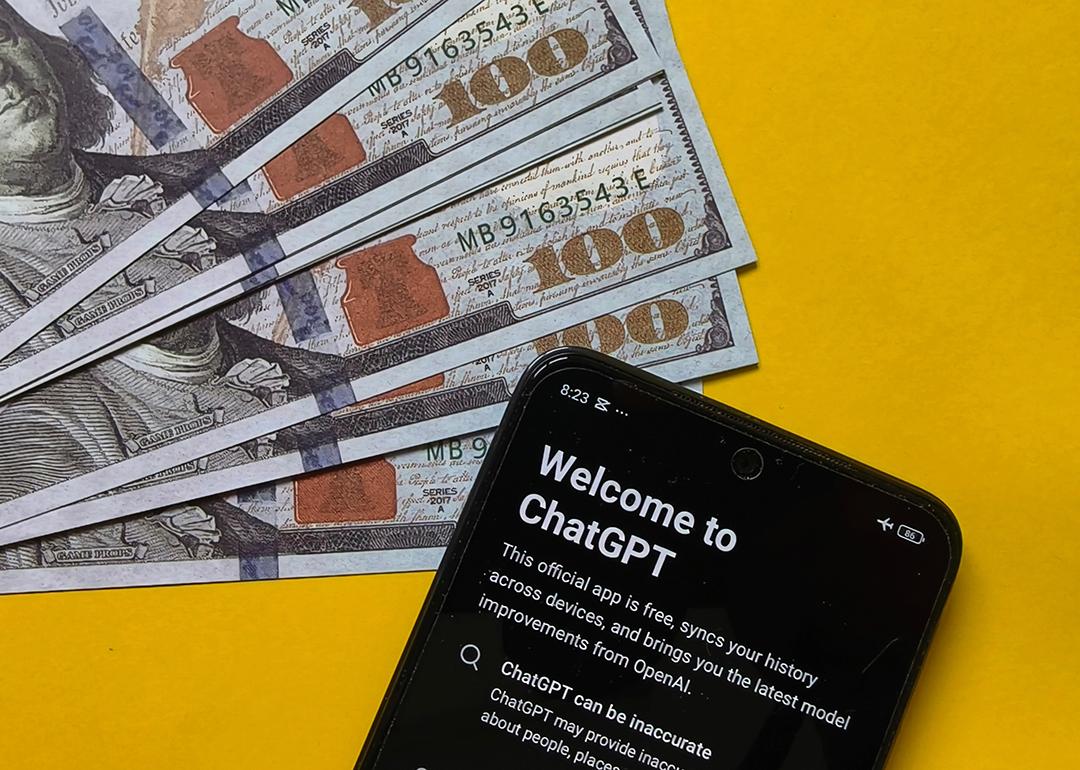 US 100 dollar banknotes and a smartphone displaying ChatGPT in a yellow background, symbolizing the concept of financial AI.