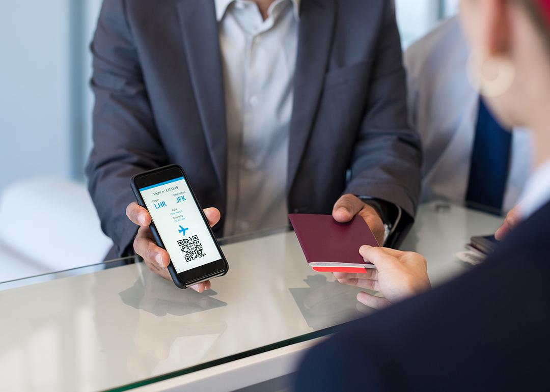 A businessman showing passport and flight ticket using his smartphone at airport check-in.