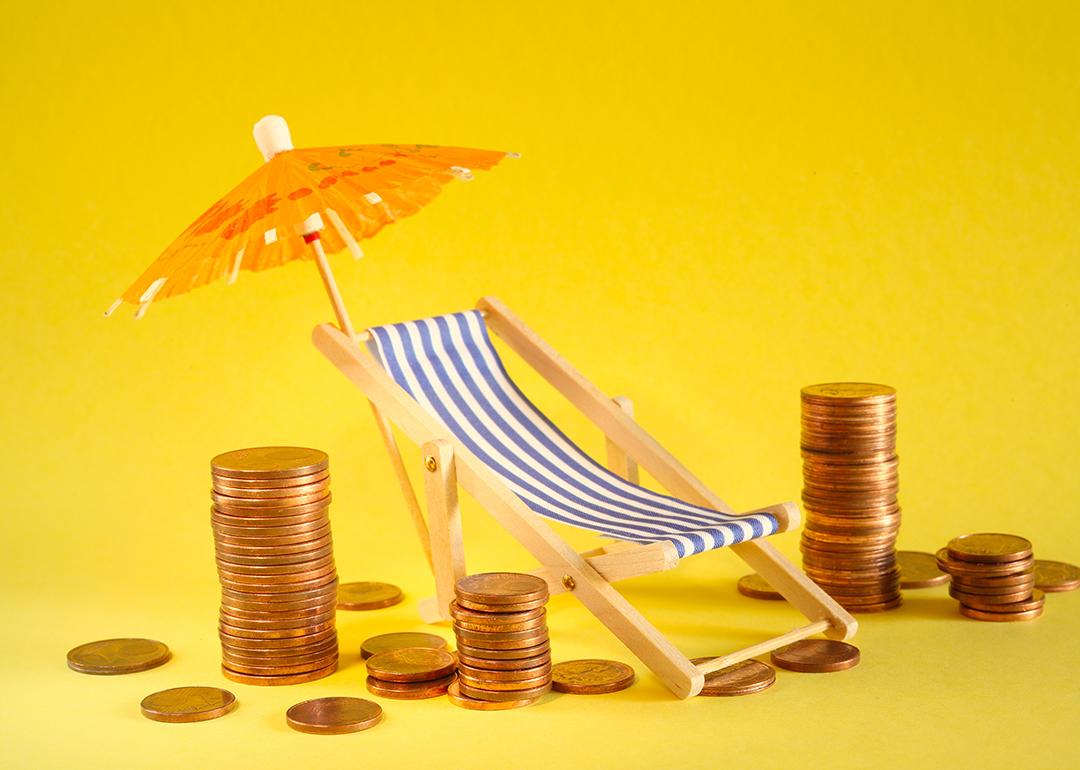 Coins around a beach deck chair and umbrella as a concept of saving for a holiday.