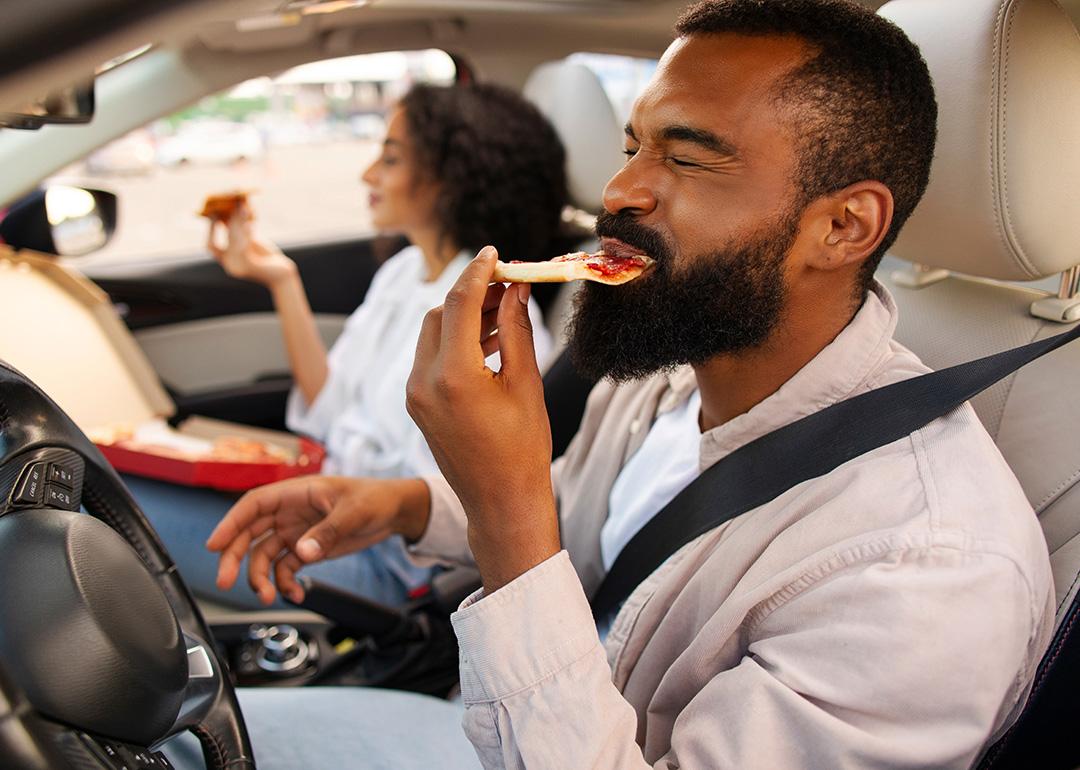 A couple eating pizza in the car during a road trip.
