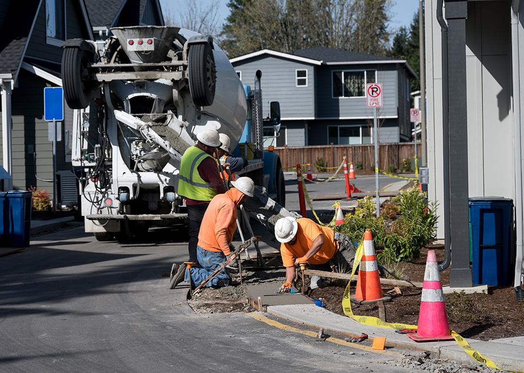  A group of construction workers smoothening a wide concrete curb.