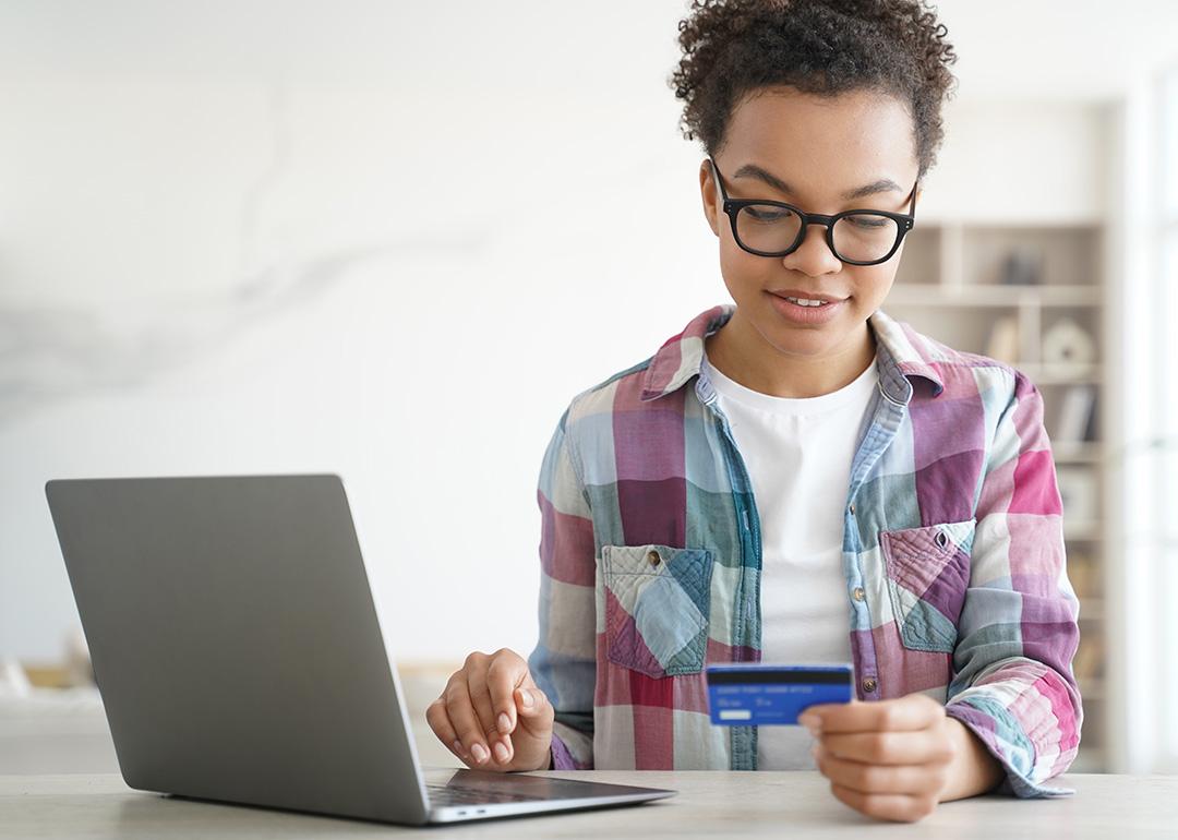 A teenager holding a credit card while shopping online from a laptop.
