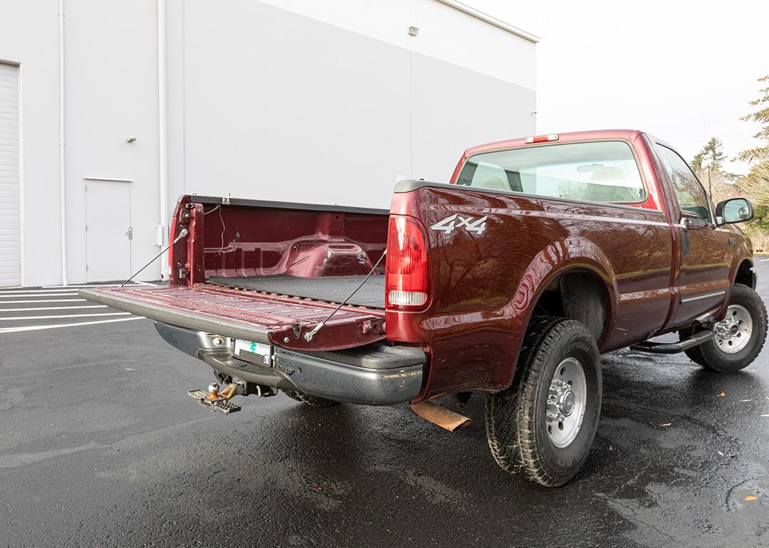 A burgundy 2000 Ford F-250 Super Duty pickup truck parked in an outdoor garage with its tailgate open.