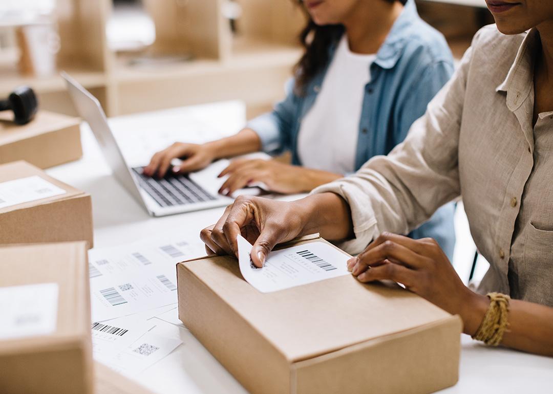 A store owner sticking a barcode label into a package box in an office warehouse.