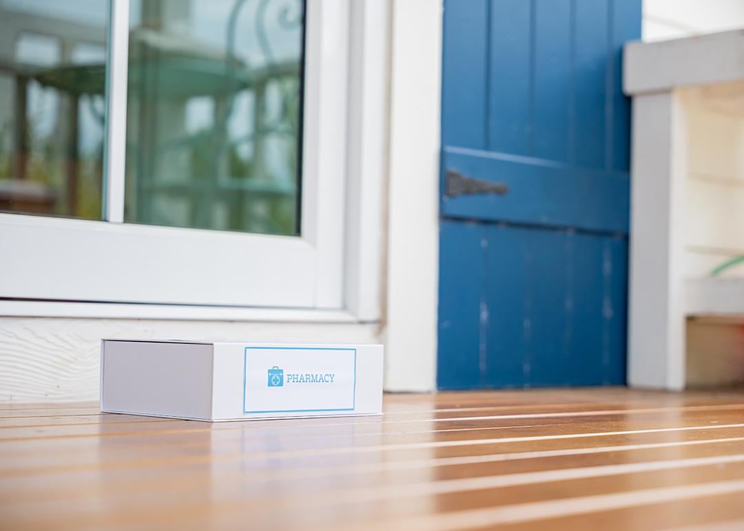 A package box labeled from pharmacy left on the front porch of a house as a delivery.