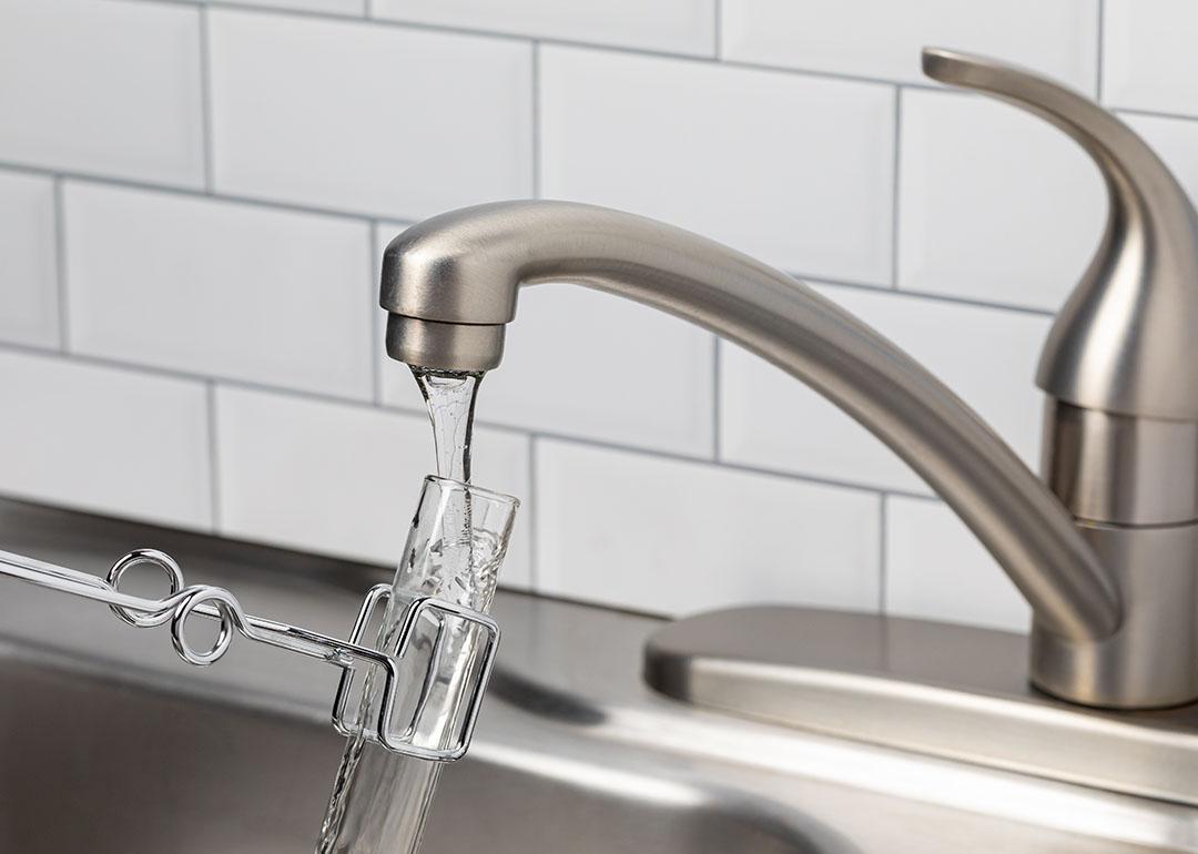 A tube test placed under the tap to collect a water sample from a kitchen faucet.