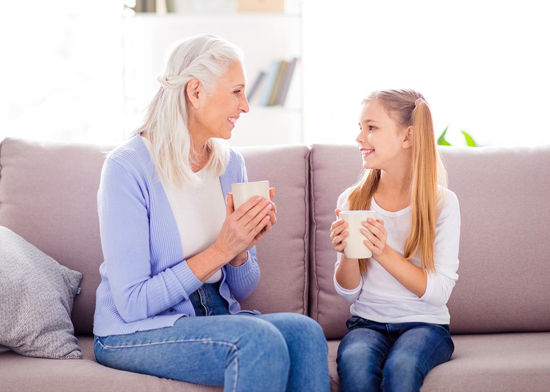 A mother and her young daughter enjoying a hot drink on the sofa.