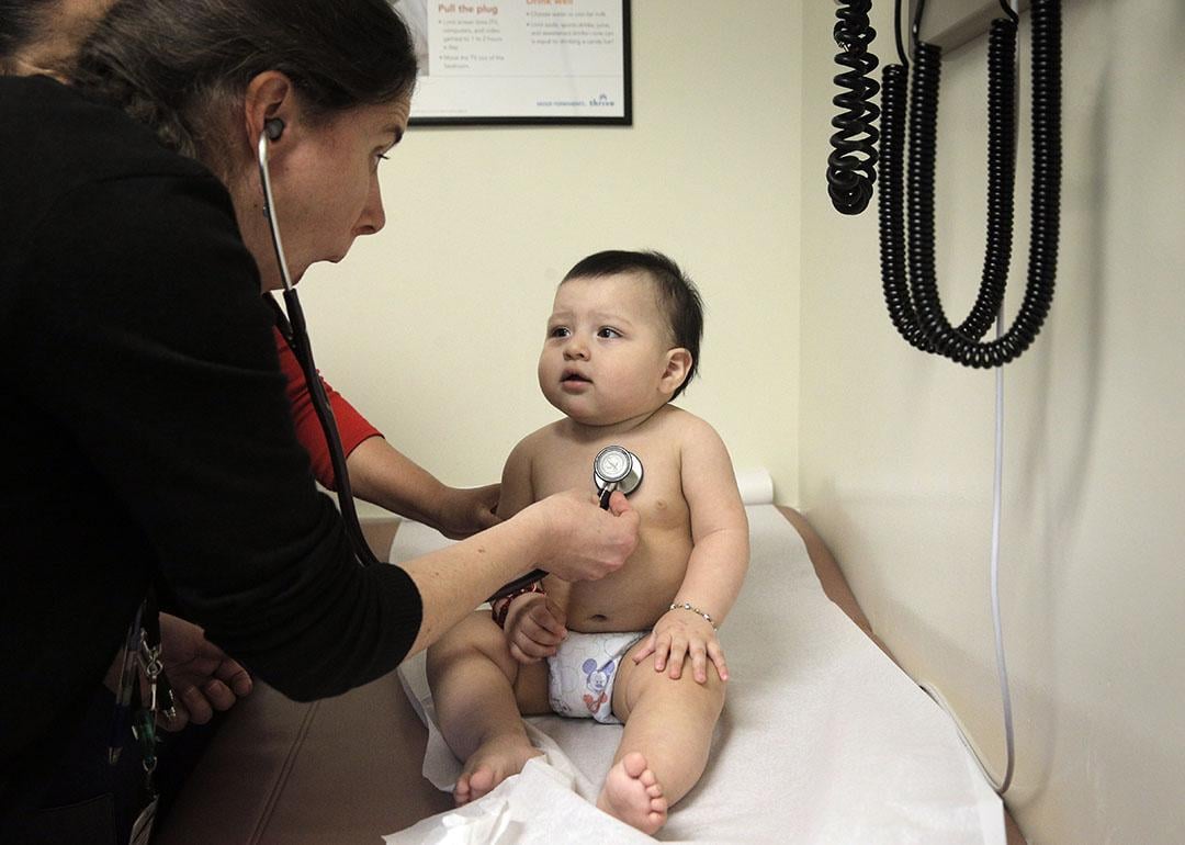 A pediatrician distracts a 9-month-old boy to check his heartbeat.