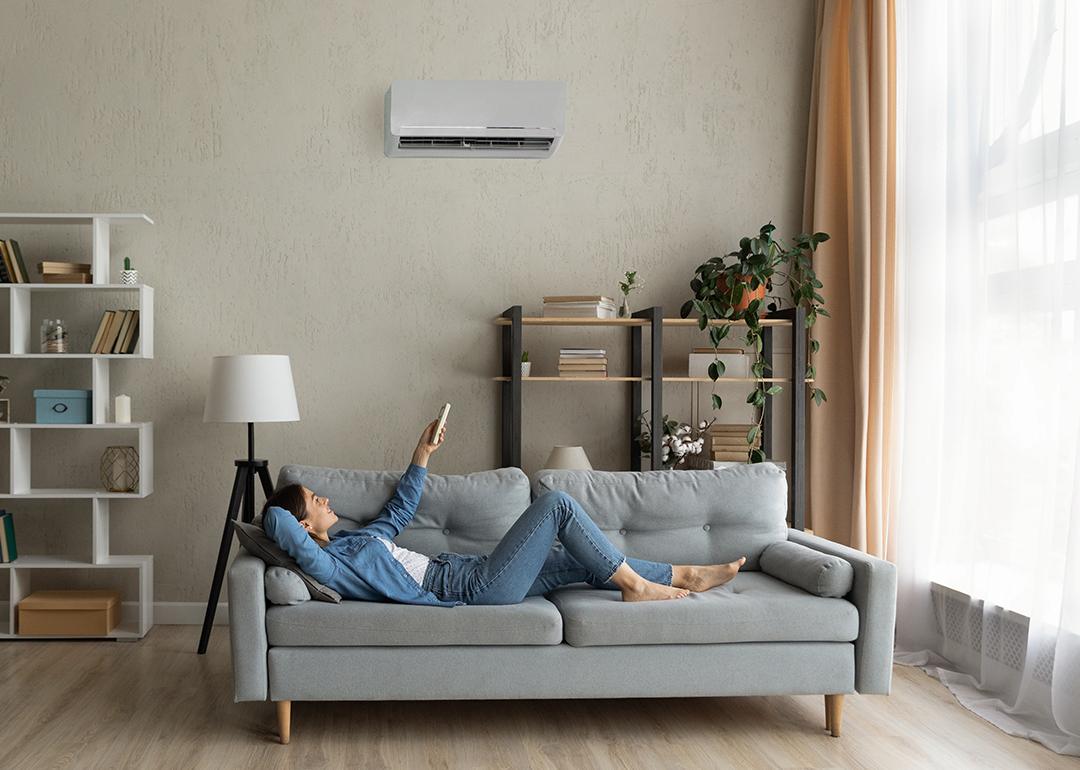 A young woman at home relaxing on the sofa and turning up the AC temperature.