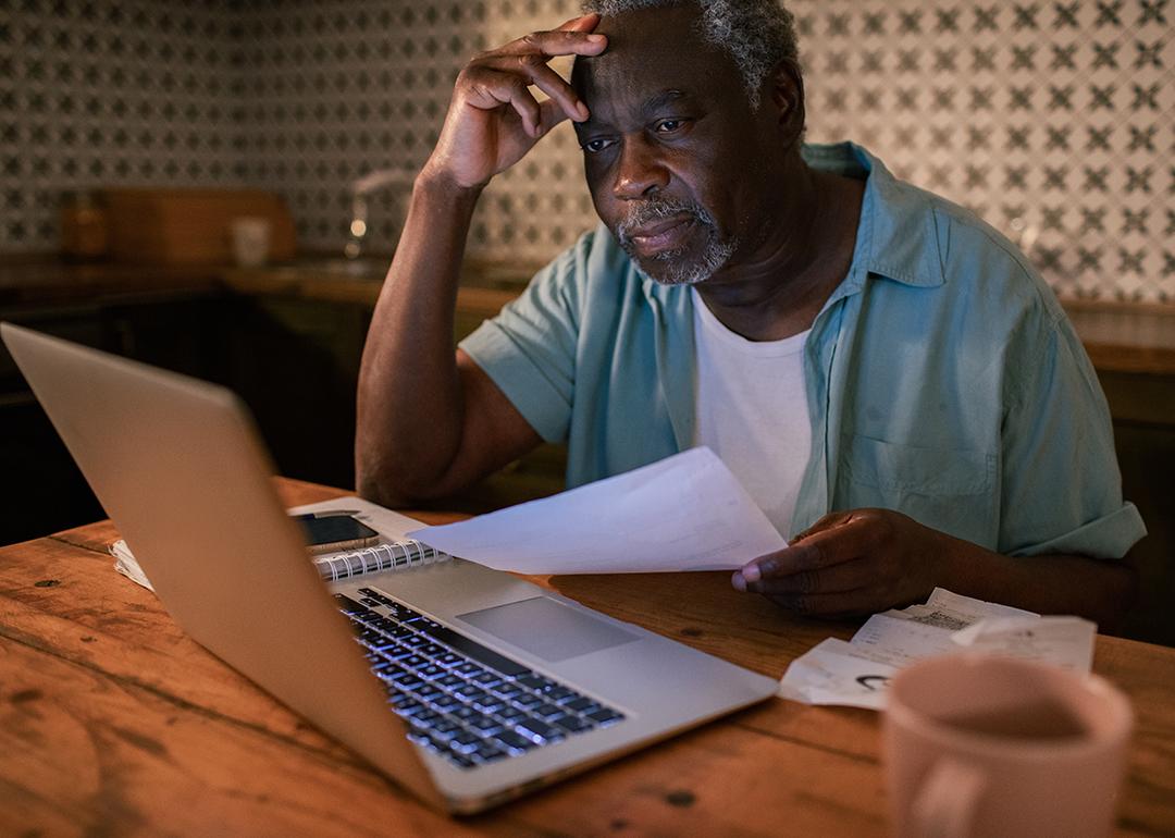 An elderly man reviewing his budget and finances from a laptop at home.