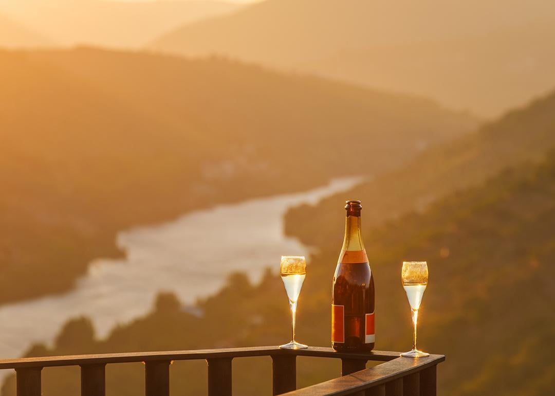 A bottle of wine and two glasses on a balcony rail with the view of the Douro Valley in Portugal.
