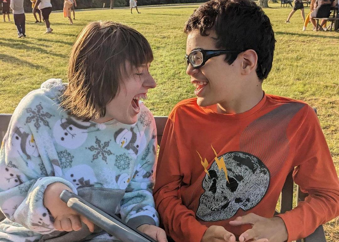 Two young individuals with disabilities happily engaging in a conversation outdoors.
