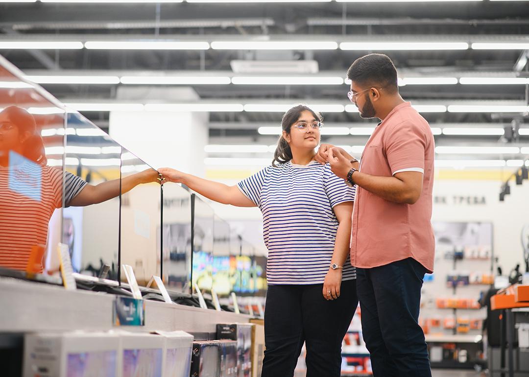 A young couple at an appliance store contemplating to buy a new flatscreen TV.