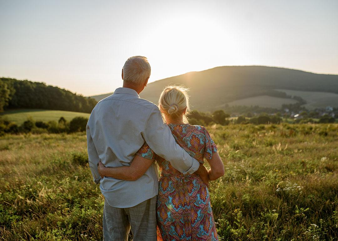 An elderly married couple enjoying the sunset view after a walk.