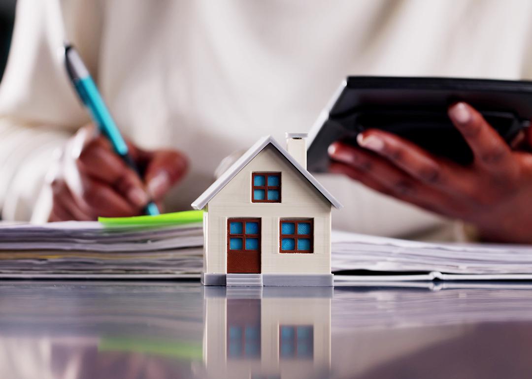 A small figure of a home with a real estate professional calculating finances in the background.