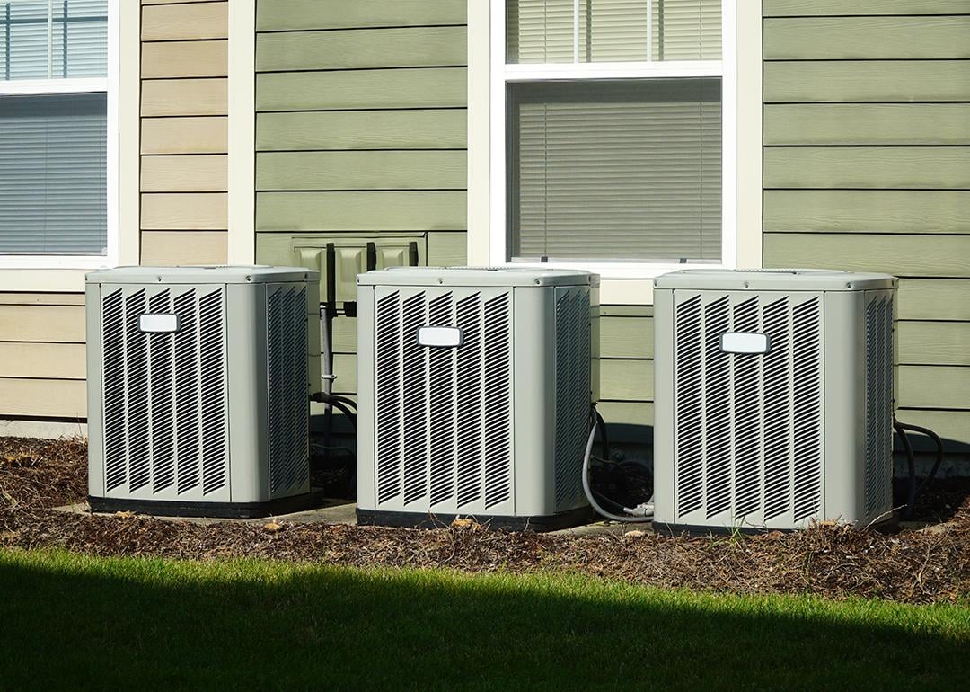 Three air conditioner compressor units placed behind a house.