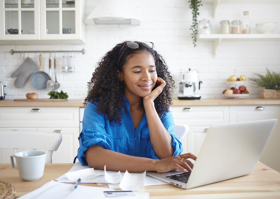 A young woman paying bills online in her home kitchen.