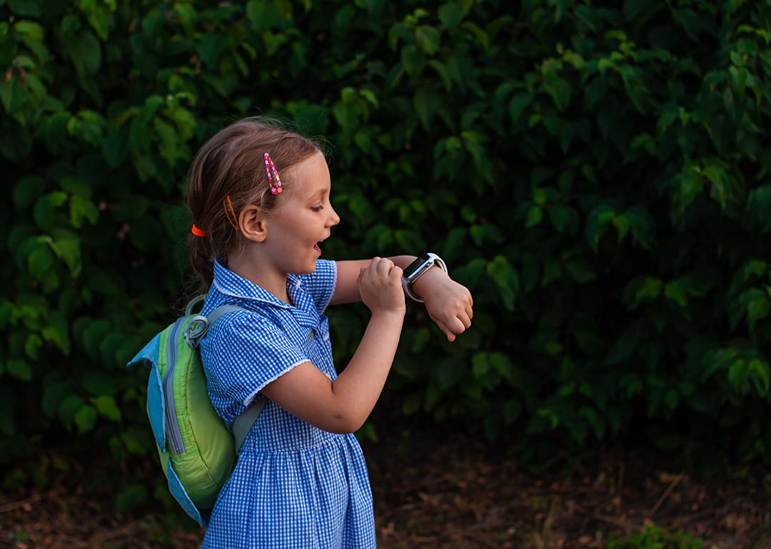 A school kid using her smartwatch outdoors in a park.