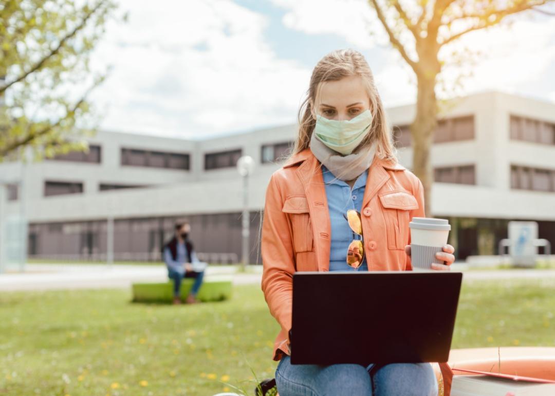 A woman wearing a mask while on a computer.